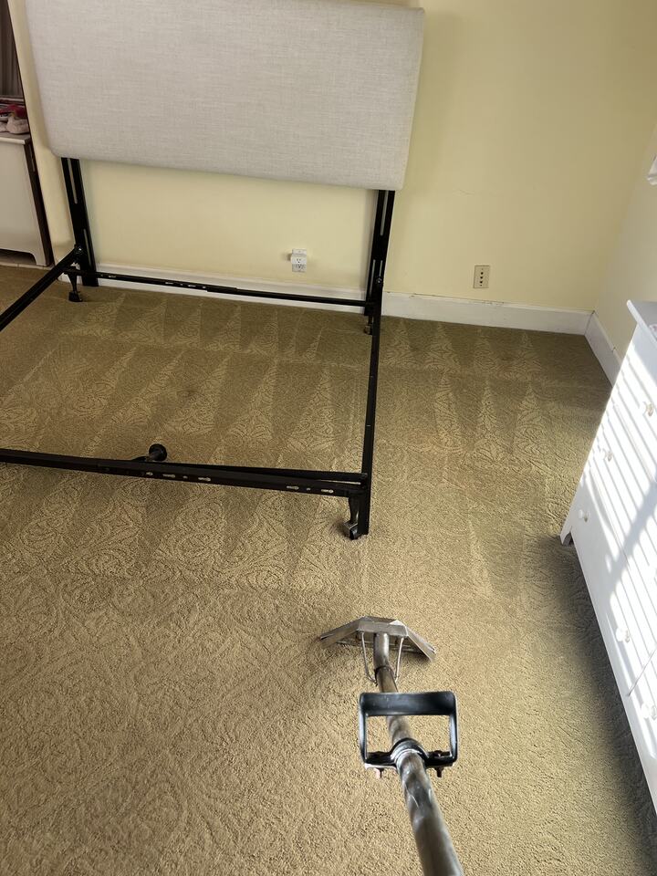 Cleaning wand on carpet around a furniture frame